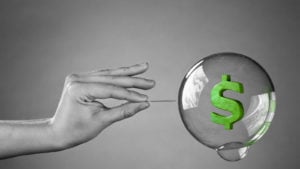 black and white photo graphic of hand holding a pin up close to a floating bubble. The bubble has a green dollar sign inside of it.