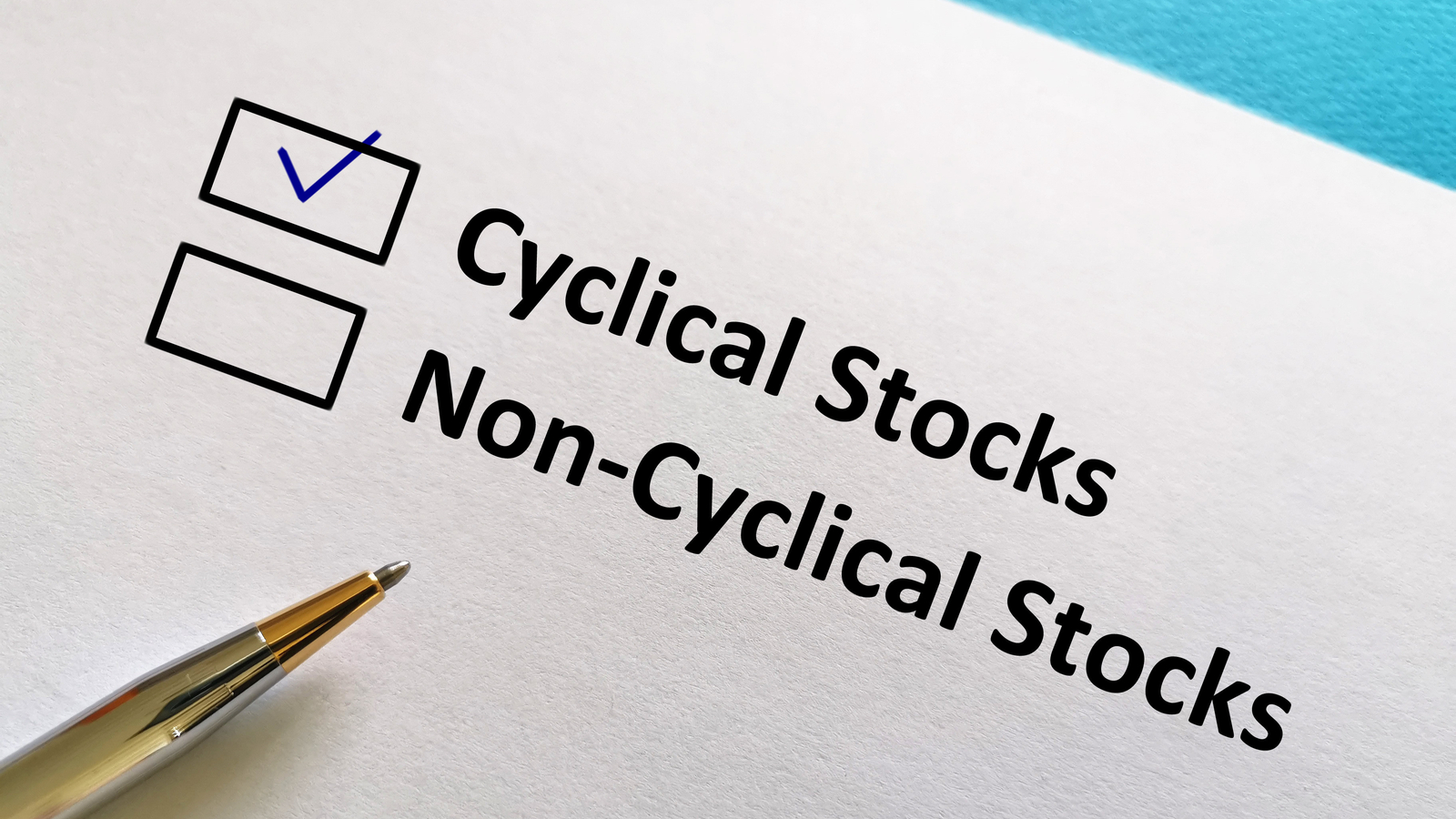The phrases 'Cyclical Stocks' and 'Non-Cyclical Stocks' are printed on a piece of paper with boxes next to them. A check mark has been drawn in the Cyclical Stocks box, and a pen rests on the paper.