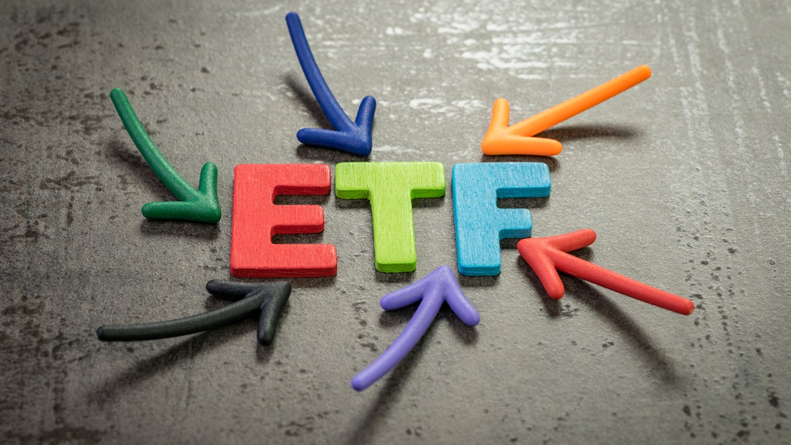 Colorful arrows pointing at the multicolored word "ETF" against a cement surface