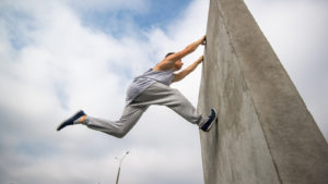photo of man practicing parkour, jumping on tall cement wall in black sneakers