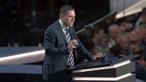 A shot of Peter Thiel at a podium with a crowd in the background.