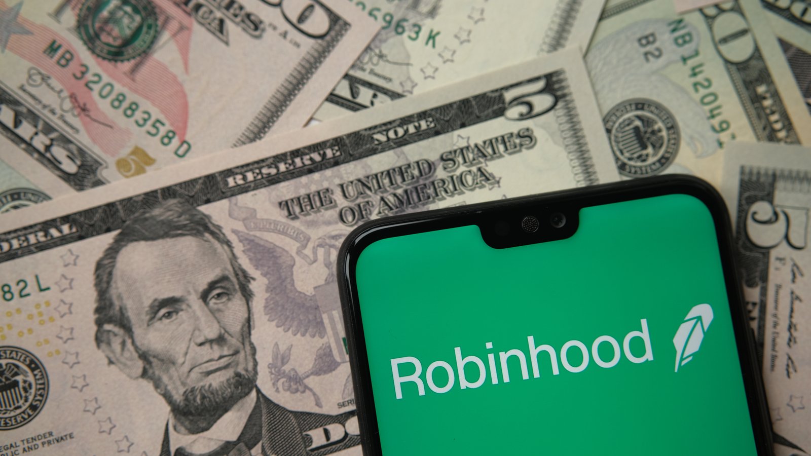 Robinhood app logo seen on smartphone on US dollar banknotes representing hood stock.