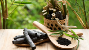 A basket of bamboo charcoal and a paddle of bamboo charcoal powder are on a table in an outdoor environment.