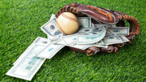 A baseball glove rests on a field with a baseball and several hundred dollar bills inside.