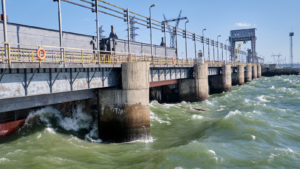 A hydroelectric power plant operates in a river with large waves crashing against the side.