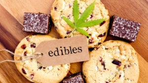 Several marijuana cookies and brownies are on a wood surface with a marijuana leaf and a tag with the word 'edibles' resting on top.