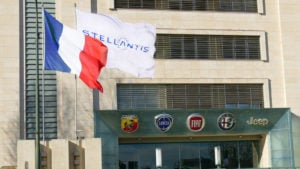 A flag bearing the Stellantis logo flies in front of a building bearing the logos of some of its car brands, including Abarth, Lancia, Fiat, Alfa Romeo and Jeep.