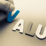 Value stocks: A hand places wooden cutouts of the letters in the word "value" on a surface.