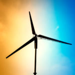 A wind turbine appears in silhouette against a bright orange and blue sky.