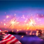 Usa Celebration With Hands Holding Sparklers And American Flag At Sunset With Fireworks