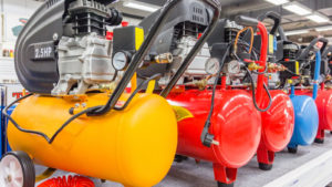 A row of yellow, red and blue air compressors are lined up next to each other.