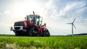 An electric tractor sits in a field on a sunny day with a wind turbine in the background.