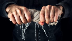 Man squeezing water out of a rag representing PTPI Stock.