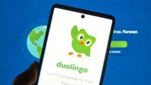 DUOL ストック: Duolingo サイトが表示されているコンピューター画面の前に、duolingo のロゴが表示されている携帯電話