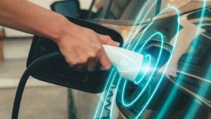 A hand holds an electric vehicle battery charger up to a car representing EV Stocks Outlook for 2022.