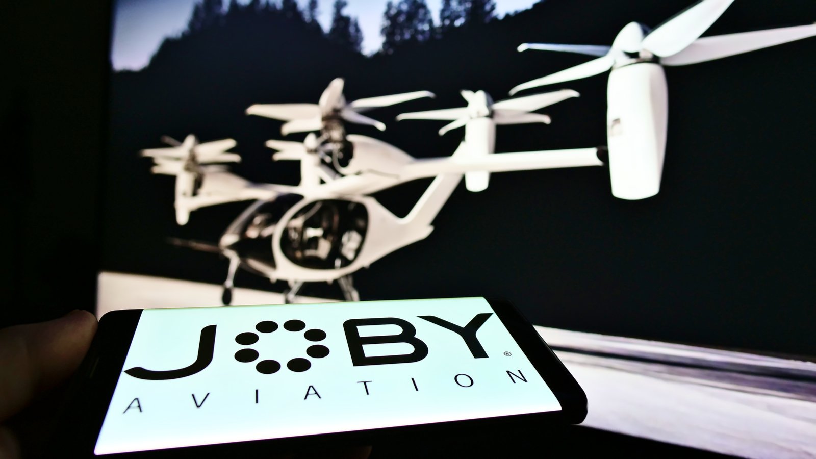 Person holding smartphone with logo of startup and aerospace company Joby Aviation (air taxi) on screen JOBY stock.