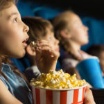 girl looking fascinated eating popcorn watching a movie at the local movie theatre. Best movie stocks to buy
