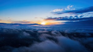 A photograph of the sun setting from a vantage point above the clouds.