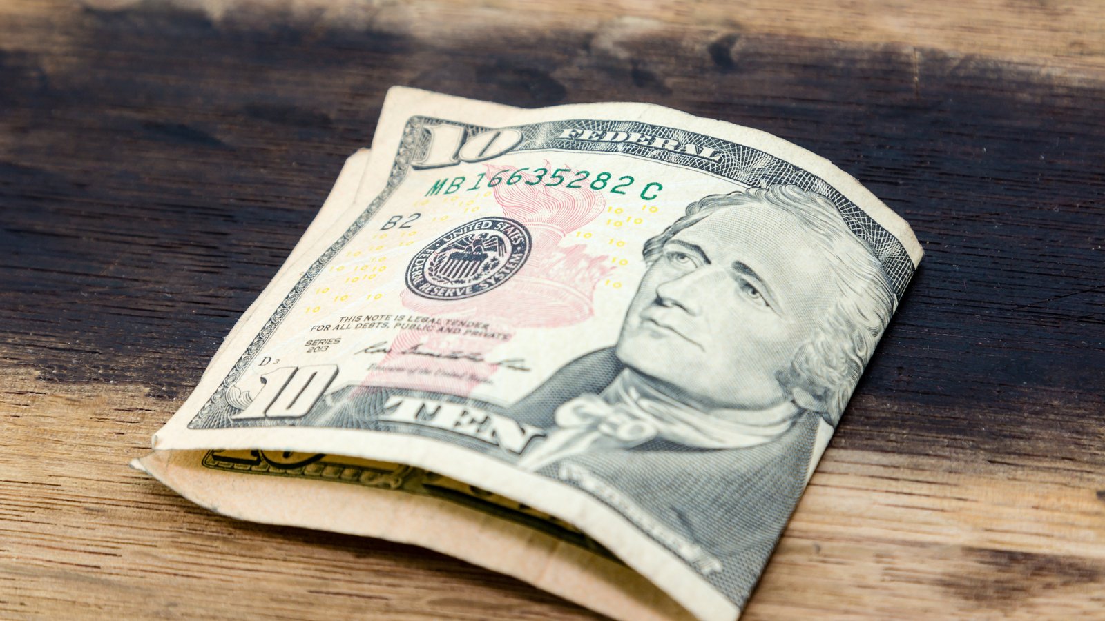 A folded ten dollar bill sits on a wooden surface.