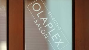 A sign for an Olaplex (OLPX) salon on a frosted glass door.