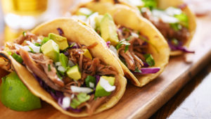 Three soft tacos stuffed with ingredients are displayed on a wooden serving tray.