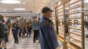 A photograph looking through a glass window as a customer shops for Warby Parker (WRBY) glasses.