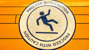 A sign with the words "proceed with caution" and an icon of a person falling is placed on an orange surface.