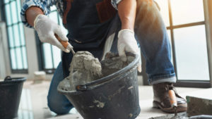 A person wearing work clothes scoops cement out of a bucket.