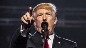 Un primer plano de Donald Trump detrás de un micrófono con un brazo extendido.