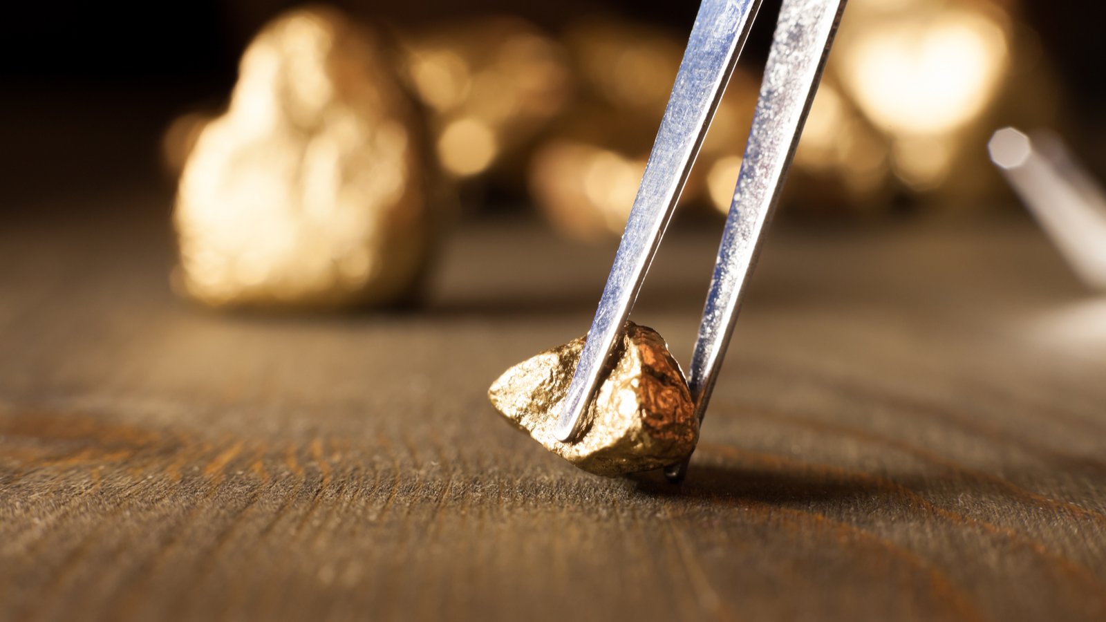 NEM Stock. A photo of a gold nugget on a table, being picked up by tweezers, with more gold behind it.