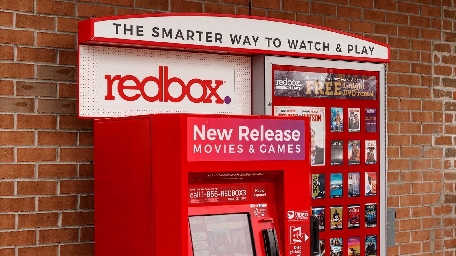 A Redbox (RDBX) kiosk in front of a brick wall.