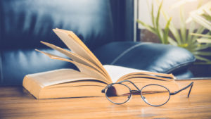 A photograph of a pair of reading glasses placed next to a book on a table.