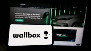 An iPhone screen with the Wallbox (WBX) logo on it in front of a computer screen.