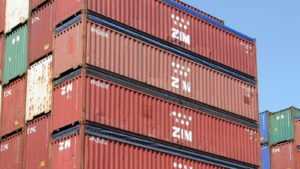 A number of shipping containers with the ZIM Integrated Shipping Services logo on the side are stacked on top of each other.