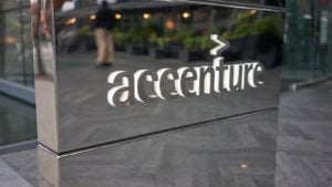 A photo of the Accenture (ACN) logo in silver and white on a silver, reflective wall outside a building.