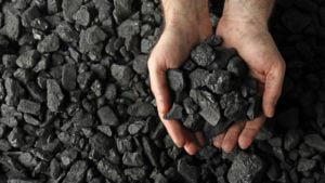 A man holds coal in his hands above a pile of coal.