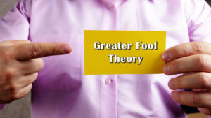 A photo of a person holding a piece of paper with "greater fool theory" written on it.