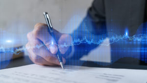 A concept image of a person signing a document with blue lines representing a stock chart in front.