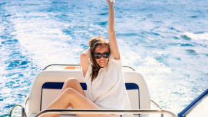 woman smiling with hand raised while riding in sporty boat on water