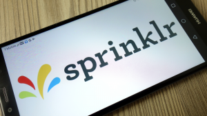 The Sprinklr (CXM) logo on a smartphone sitting on a wood table.