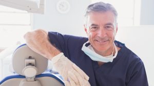 Close up of smiling dentist leaning against dentists chair in dental clinic