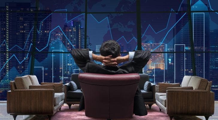 An image of the back view of a business man sitting looking at a stock chart displayed on the window