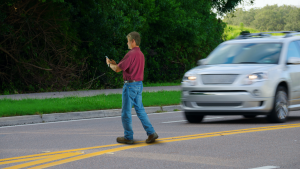 A photo of a jaywalking person looking at a phone as a car approaches.