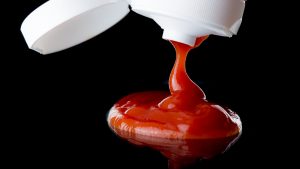 A photo of ketchup being squeezed out of a bottle onto a reflective black surface.