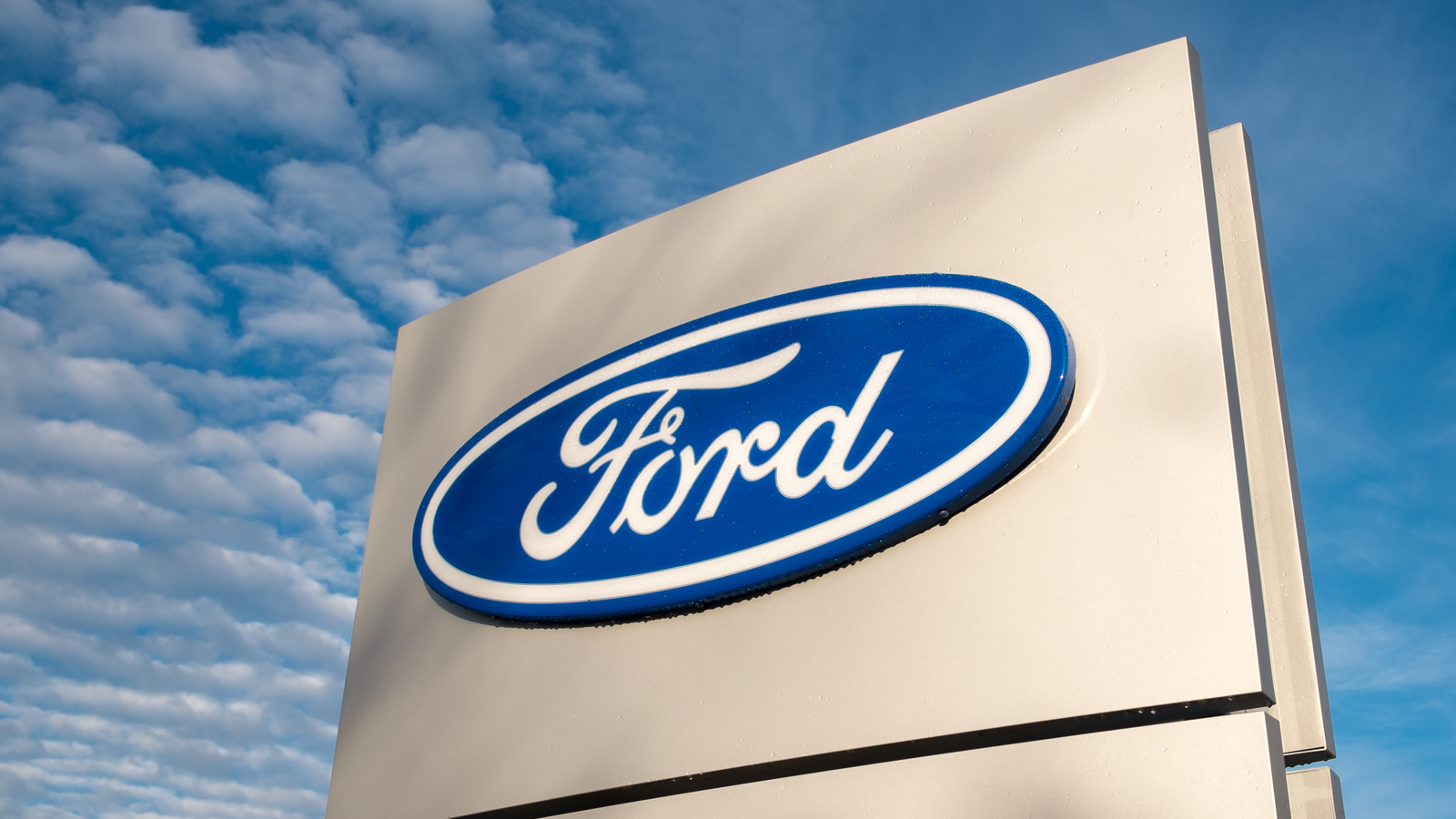 Ford (F) dealership sign against a blue sky.