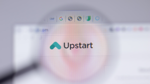 The website for Upstart (UPST stock) is viewed through a magnifying glass focused on the company's logo.