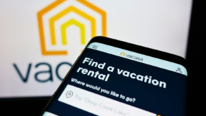 photo of Vacasa (VCSA) site open on mobile phone with words "Find a vacation rental" displayed, Vacasa logo on display in background of photo