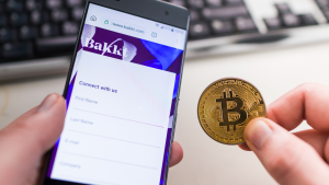 Man holding Bitcoin coin and in other hand smartphone with opened Bakkt website.
