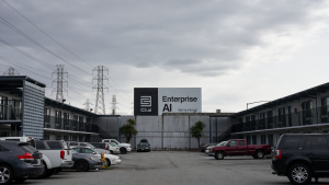 Cars in a parking lot against a gray cloudy sky with a billboard for C3.ai with company logo