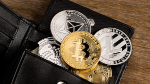 A photo of various crypto coins coming out of a black leather wallet on a wooden surface representing Stocktwits Crypto Trading Platform